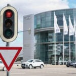 Konttorirakennus, jonka edessä liehuu lipputangoissa rivi lippuja. Rakennuksen edustalla on henkilöautoja. Etualalla on liikennevalot ja väistämisvelvollisuudesta kertova kolmion muotoinen liikennemerkki.