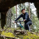 Sivulle katsova nainen istuu maastopyörän päällä metsässä.