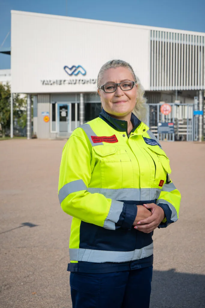 Nainen seisoo työvaatteet päällään tehtaan edustalla.