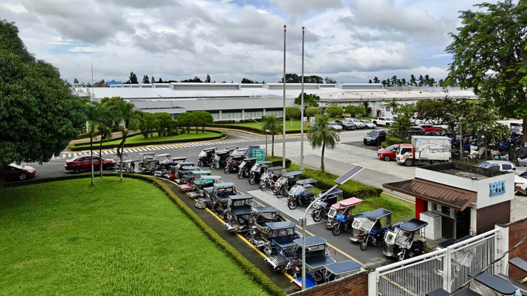 Tehdasympäristö, jonka pihalla on autoja ja mopoja.