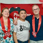 Kolme henkilöä seisoo rivissä kädet toistensa olkapäivällä. Takana on ammattiyhdistyksen punalippu.