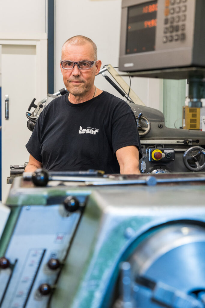 Henkilö katsoo kameraan suojalasit päässä. Hänen ylävartalonsa näkyy sorvin takaa.