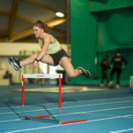 Aitajuoksija hyppää aidan yli sisäharjoitusradalla.