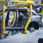 Autotehtaalla mekaaninen laite nostaa henkilöauton keskeneräistä koria.