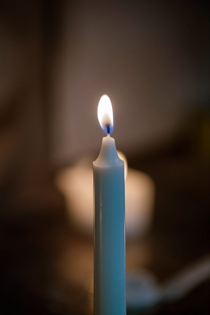 Kynttilässä palaa tuli. Liekki erottuu hyvin tummaa taustaa vasten.