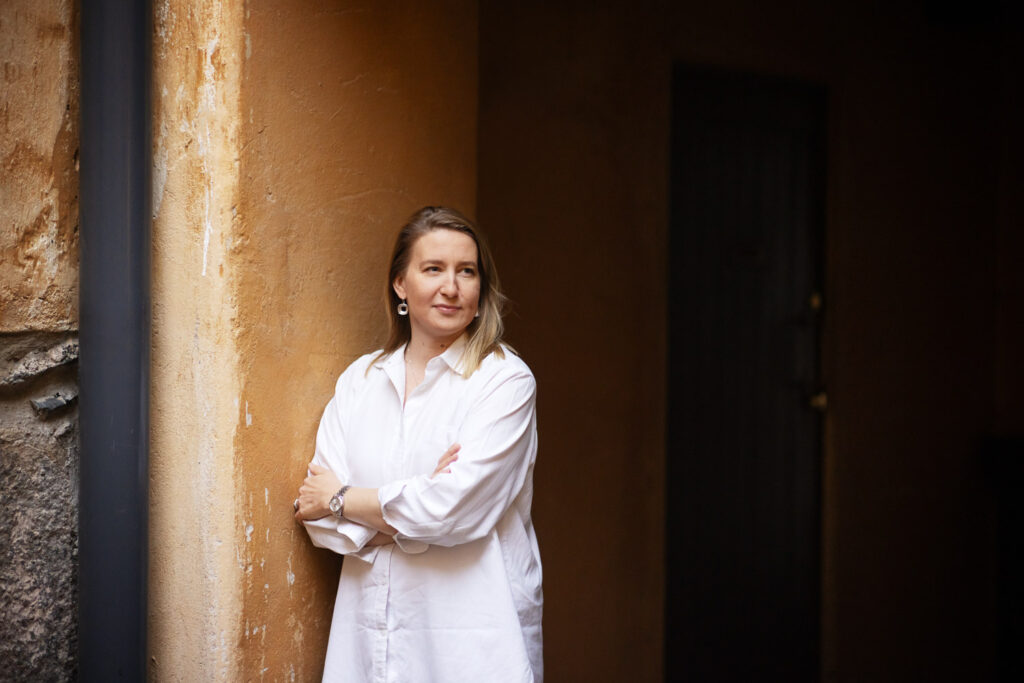 Henkilö nojaa kiviseinään ja katsoo kameran ohi yläviistoon.