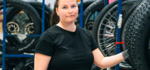 En kvinna iklädd svart t-skjorta tittar mot kameran och rör vid ett cykeldäck med vänster hand.