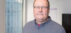 Sisätilassa läheltä kuvattu henkilö katsoo kameraan. Taustalla näkyy ikkuna.