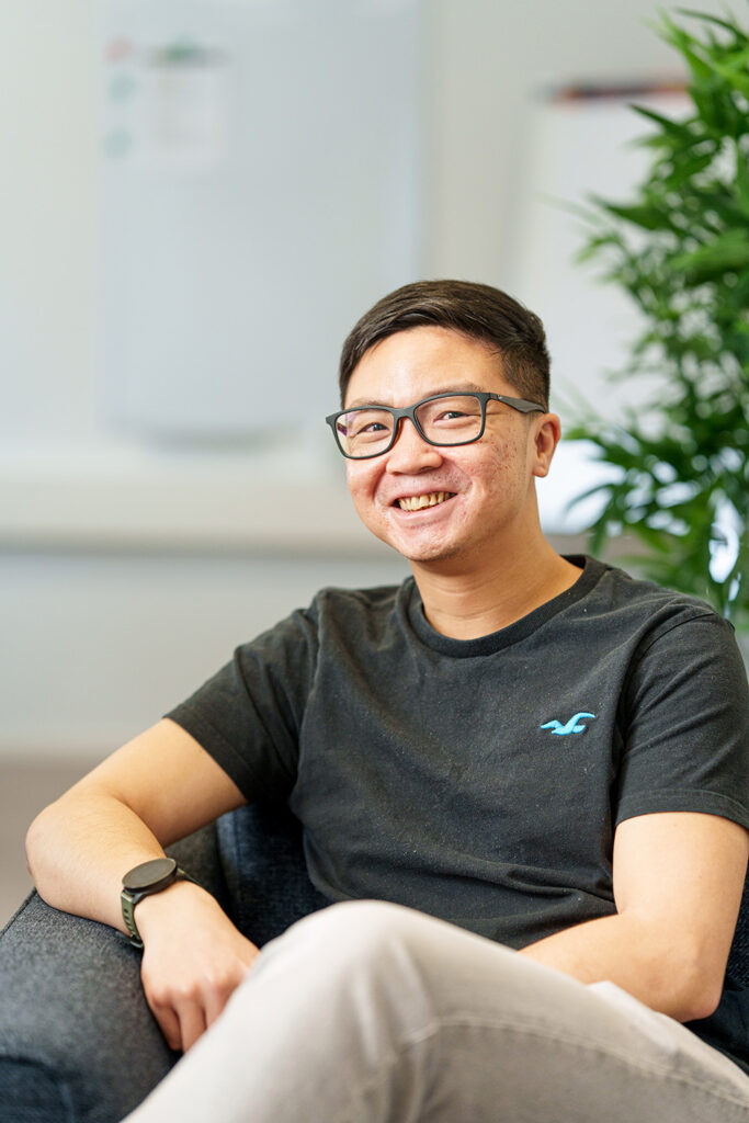 Mies istuu ja katsoo kameraan ja hymyilee.