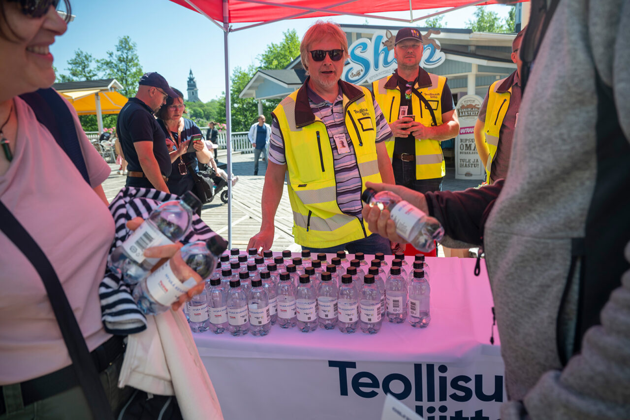 Kaksi miestä katsoo kameraan ulkoilmassa, etualalla vesipulloja.