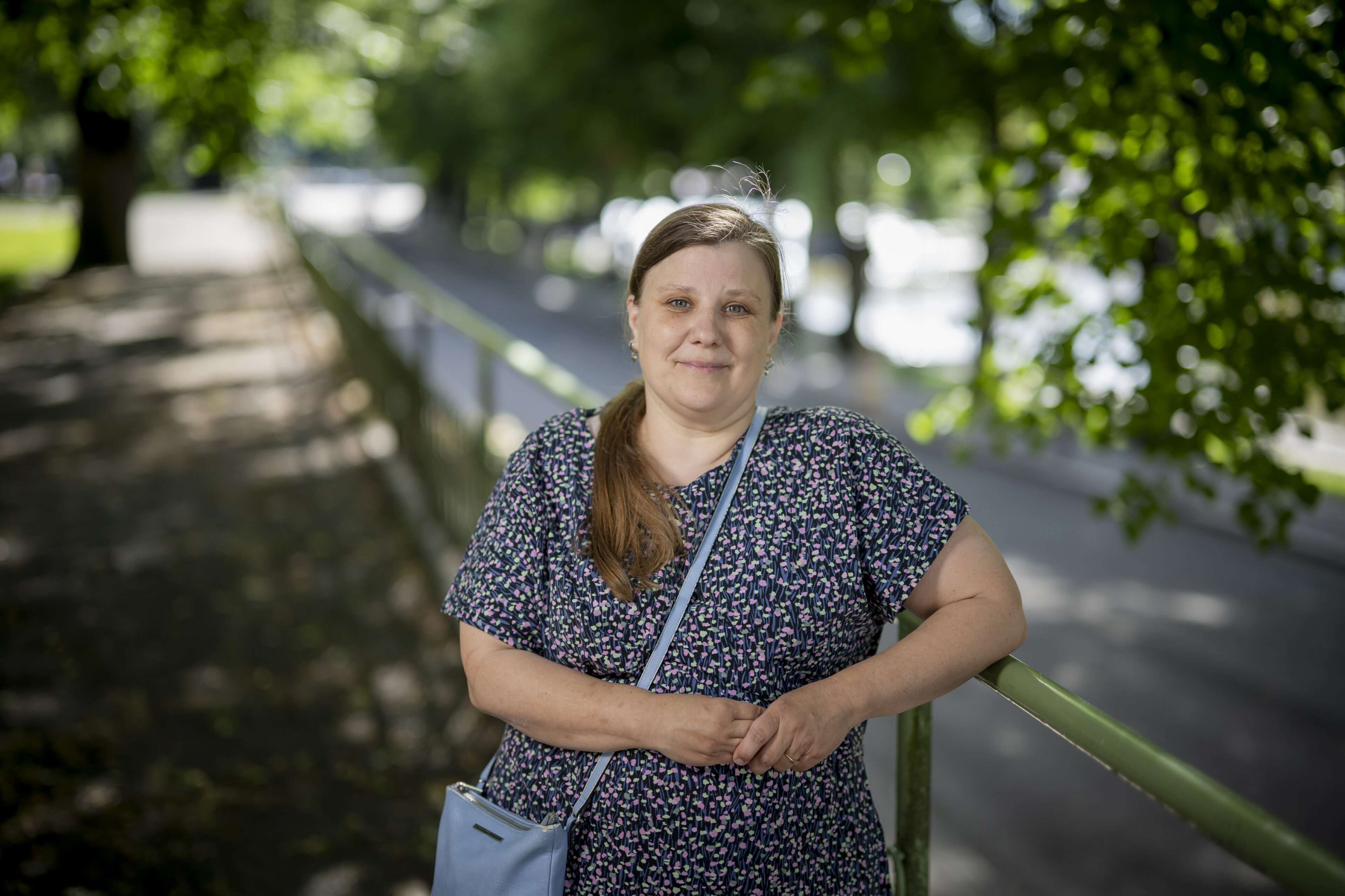 En kvinna står vid räcke och tittar rakt in i kameran. 