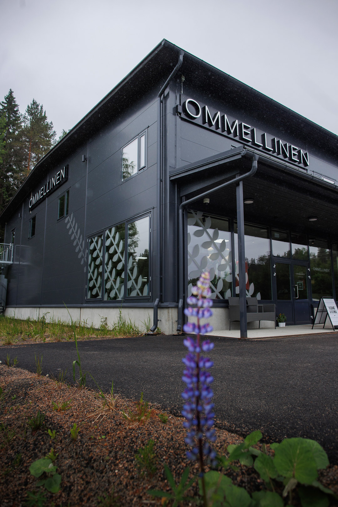Kaksikerroksinen halli, jonka seinässä lukee "Ommellinen". Kuvan etualalla on pitkulainen kukka.