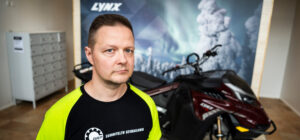 Mies seisoo moottorikelkan edessä ja katsoo kameraan